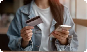 A person holding a credit card and smartphone to redeem digital gift cards online, showing the process of entering codes securely through mobile or app stores.